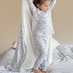 Child in pajamas playing with a white sheet on a bed