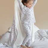 Child in pajamas playing with a white sheet on a bed
