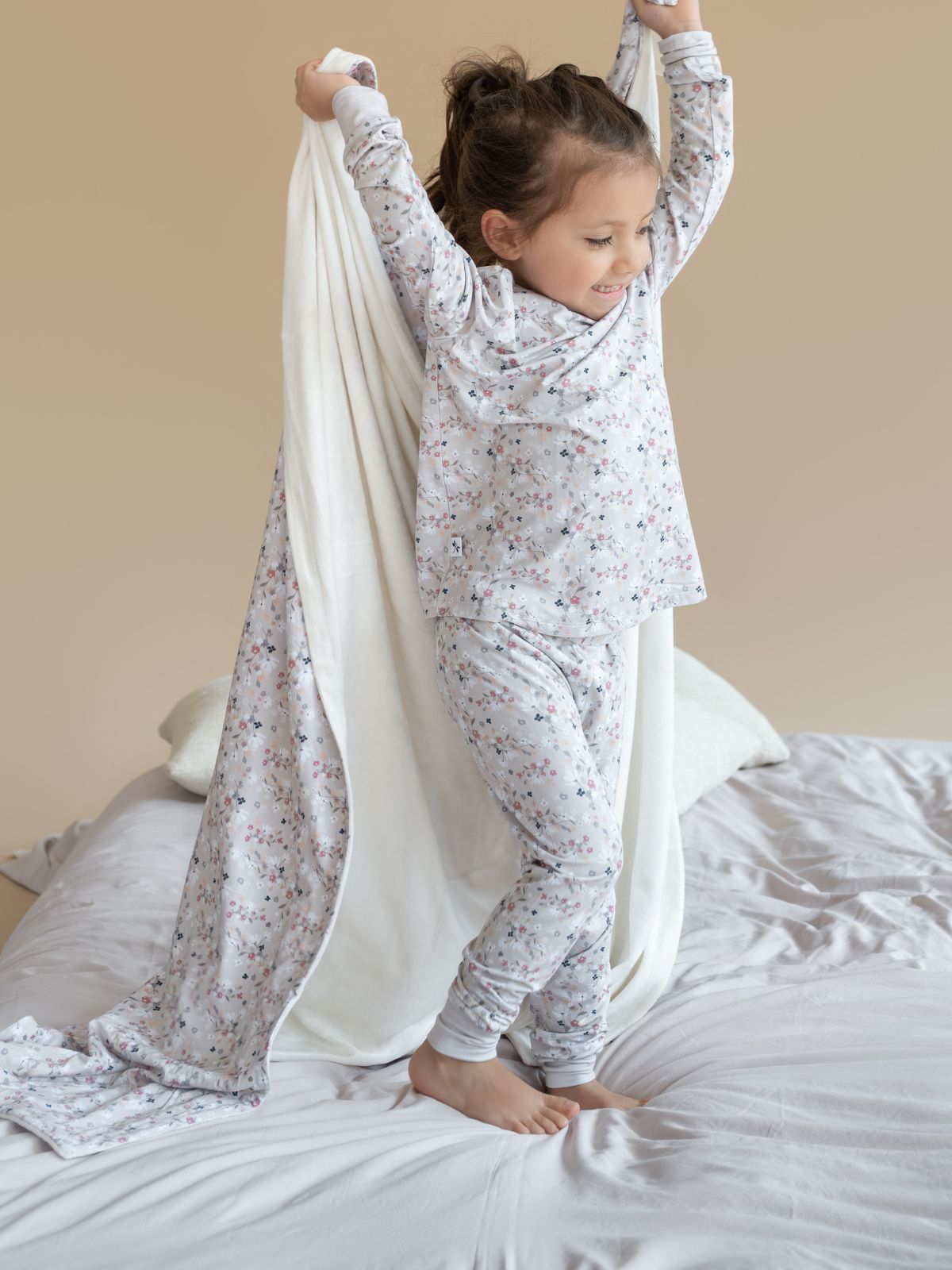 Child in pajamas playing with a white sheet on a bed